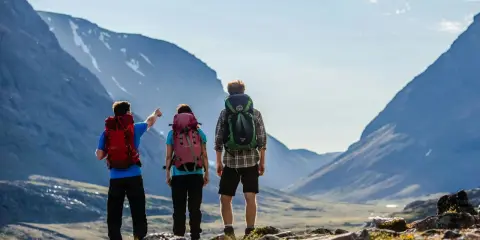 Två vandrare med ryggsäckar blickar ut över en dal under en kungsleden vandring. En pekar mot bergen.