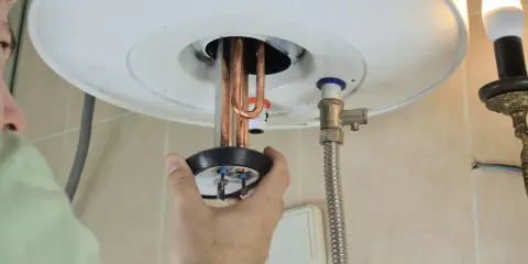 Mano ajustando la resistencia termoeléctrica de un calentador de agua.
