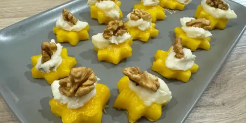 Stelline di polenta dorata con crema bianca e noci, perfetti antipasti di Natale per un tocco di sapore e colore.