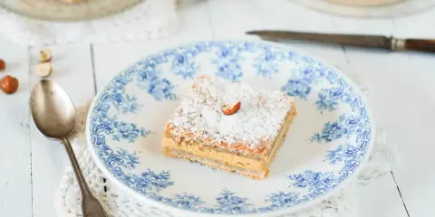 Un carré de gâteau russe, saupoudré de sucre glace et garni d'une noisette, sur une assiette ornée de bleu.