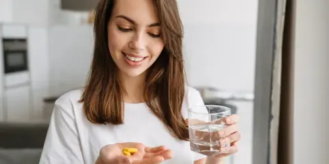Uśmiechnięta kobieta trzyma w dłoni tabletki preductal mr 35 mg i szklankę wody.