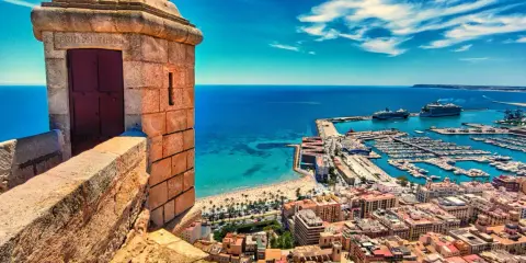 Widok z zamku na port i plażę w prowincji Alicante. Widać łodzie, statki wycieczkowe i turkusowe morze.