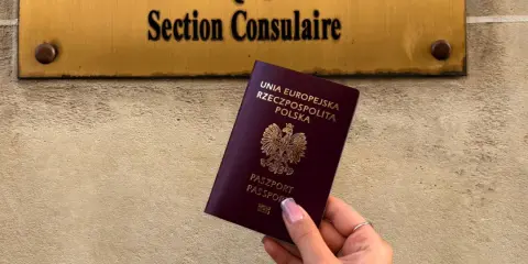 Dłoń trzyma polski paszport na tle tablicy z napisem "Section Consulaire".