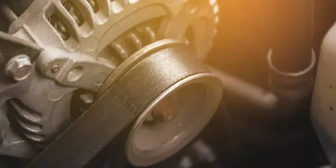 Zbliżenie na spalony alternator samochodowy z widocznym paskiem klinowym.