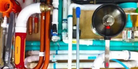 Un réseau complexe de tuyaux blancs, orange et turquoise, avec un outil de plomberie et un manomètre. Un **profilé souple** orange se courbe gracieusement.