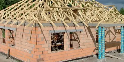 Budowa domu z cegły, na którym widać drewniany dach kopertowy w trakcie konstrukcji.