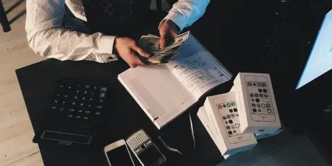Mężczyzna liczy pieniądze, obok leżą telefony i kalkulator. To może być pomocne, jak udowodnić pochodzenie pieniędzy.