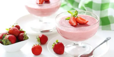 Deliziosa mousse di fragole in coppette di vetro, guarnita con fragole fresche e menta. Accanto, fragole in una ciotola bianca.