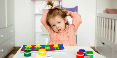 Bambina con puzzle e colori, un'immagine che fa riflettere su cos'è l'asperger e come supportare i bambini.