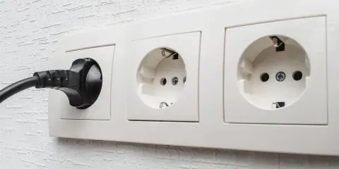Une prise C16 noire est branchée dans une prise murale blanche. Deux autres prises sont visibles.