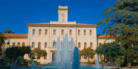 Fontana zampillante nella piazza Roosevelt di Cattolica, con un edificio giallo e un cielo azzurro.