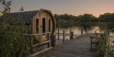 En tunnbastu vid en sjö i Sverige, med en brygga och fiskespön. Perfekt för en avkopplande stund.