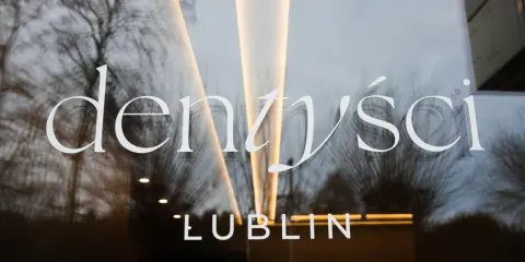 Napis "Dentyści Lublin" na szklanych drzwiach z odbiciem drzew i światła.