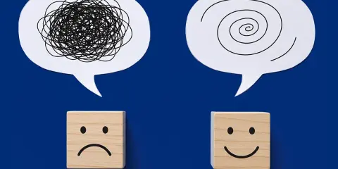 Dwa dymki myśli: jeden z chaotyczną linią, drugi ze spiralą. Pod nimi kostki z minami: smutną i uśmiechniętą. Przykłady zaburzeń emocjonalnych i ich przezwyciężania.