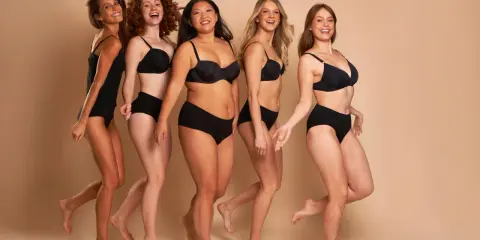 Cinque donne diverse, con taglia nona di seno e forme varie, camminano sorridenti in lingerie nera.