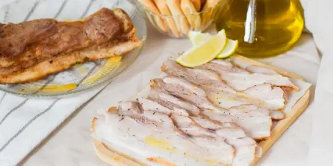 Chicharrón de Cádiz, lonchas de panceta crujiente, limones y palitos de pan, listos para disfrutar.