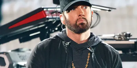 Eminem w czapce i z łańcuchem na szyi. W tle sprzęt muzyczny. Ciekawe, ile ma lat Eminem?