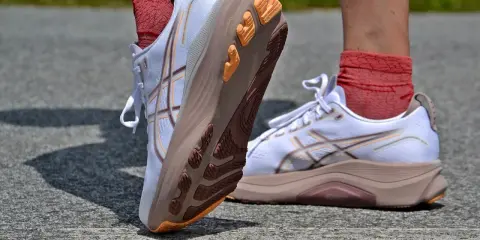 Białe buty do biegania z pomarańczowymi akcentami i charakterystycznym logo. To właśnie asics co to za firma, znana z innowacyjnych rozwiązań dla sportowców.