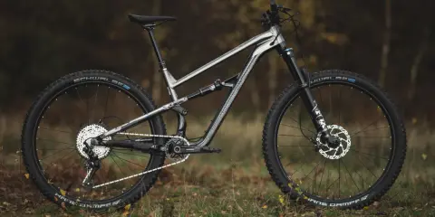Szary rower górski Polygon Siskiu T8 z pełnym zawieszeniem, gotowy na jesienne trasy po lesie.