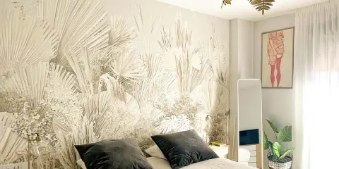 Dormitorio con papel pintado de palmeras, ideal para aprender como poner papel pintado. Cama con cojines oscuros, espejo y planta.