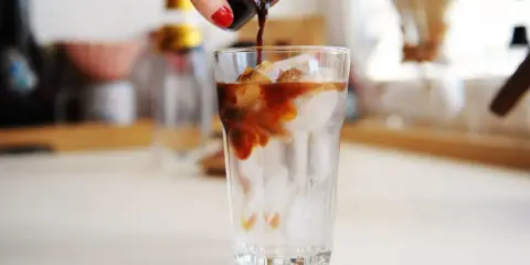 Ręka wylewa espresso na lód w szklance. Idealny napój na upalne dni - tonic espresso.