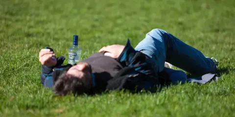 Mężczyzna leży na trawie obok butelki wódki. Czy padaczka alkoholowa jest śmiertelna? To pytanie budzi niepokój.