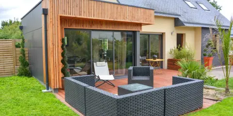 Une extension bois 30m2 moderne avec terrasse en bois, mobilier de jardin et grandes baies vitrées.
