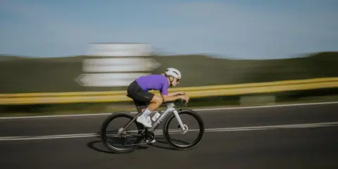 Kolarz w fioletowej koszulce pędzi na rowerze, osiągając prędkość 50 km/h.