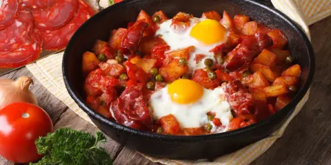 Pyszne danie z jajek na obiad: ziemniaki, chorizo, papryka i groszek zapiekane w patelni.