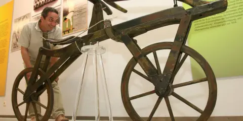 Mann betrachtet ein hölzernes Laufrad, den Vorläufer des Fahrrads, das von Karl Drais, dem Erfinder des Fahrrads, entwickelt wurde.