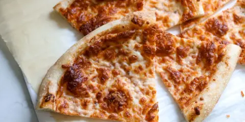 Tranches de pizza au fromage doré, préparées avec un levain rafraichi, sur du papier sulfurisé.