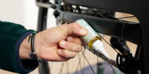 Dłoń z buteleczką oleju aplikuje go na rowerowy łańcuch, dbając o jego płynne działanie. Czyszczenie łańcucha rowerowego to klucz do sprawnej jazdy.