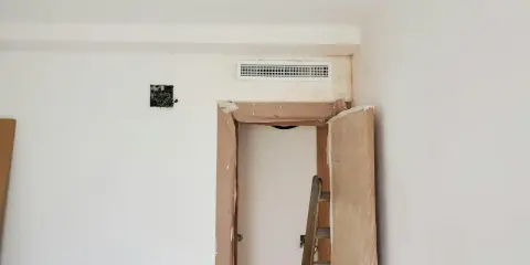 Habitación en obra con rejilla de preinstalación aire acondicionado en la pared, puerta abierta y escalera.