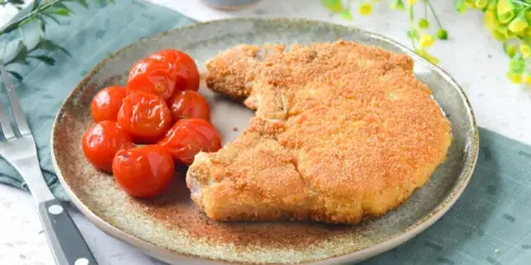 Cotoletta alla milanese dorada y crujiente, acompañada de tomates cherry asados. Un plato clásico y delicioso.