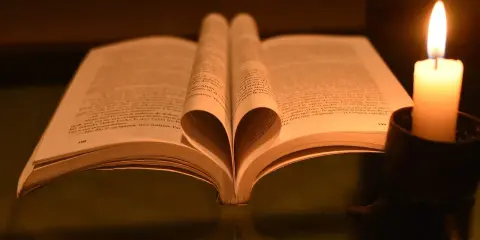 Otwarta księga z kartkami uformowanymi w serce, obok płonąca świeca. W świetle świecy czytam psalm 37 1-4.