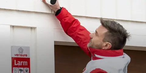Man i röd jacka monterar en Arlo-kamera för Verisure-larm.