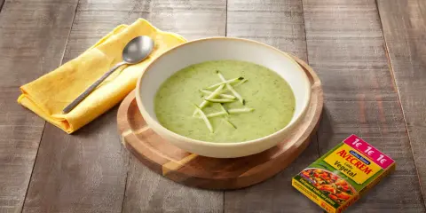 Crema de calabacín para niños, servida en un cuenco blanco sobre tabla de madera. Al lado, un paquete de caldo vegetal Avecrem.