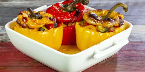 Peperoni ripieni di riso alla salentina, dorati e invitanti, in una teglia bianca su un tavolo di legno.