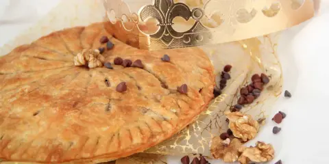 Une galette des rois pépite de chocolat dorée, parsemée de pépites de chocolat et de noix, sous une couronne royale.