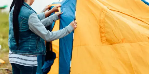 Eine Frau reinigt ihr gelbes und blaues Zelt am Seeufer.
