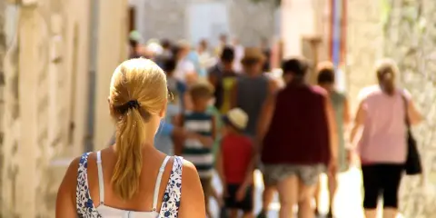 Kobieta z blond kucykiem idzie wąską uliczką pełną ludzi, odkrywając urokliwe villach atrakcje.