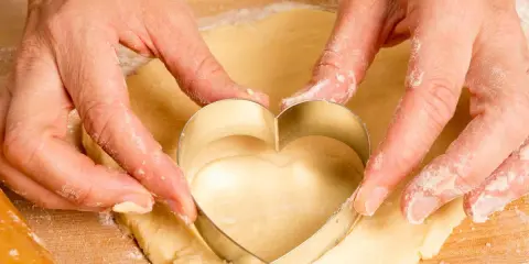 Manos cortan masa con un cortador en forma de corazón, parte de una receta de galletas caseras.