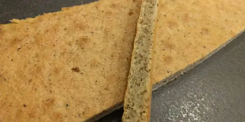 Un biscuit joconde noisette, fin et doré, est coupé en deux. Une fine tranche repose sur une plus grande pièce.