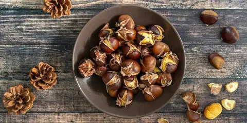 Châtaignes grillées dans un bol, sur fond de bois, avec des pommes de pin.