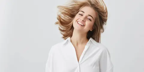 Uśmiechnięta dziewczyna z burzą blond włosów, które falują jak suche puszące się włosy.