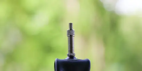Wentyl Dunlop jak pompować? Zobacz zbliżenie metalowego wentyla rowerowego na tle zieleni.