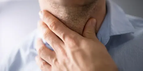 Mężczyzna trzyma się za gardło, szukając sposobów na zdarte gardło po koncercie.