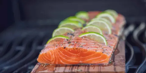 Lachs auf Zedernholz grillen, mit Limettenscheiben und Kräutern belegt. Ein saftiges Stück Fisch auf dem Rost.