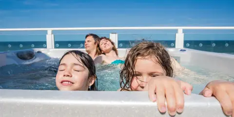 Famiglia felice in vasca idromassaggio, godendosi il Ferragosto con bambini. Il sole splende, il mare sullo sfondo.