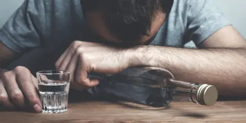 Mężczyzna z butelką alkoholu i kieliszkiem. Nadmierne spożycie alkoholu wpływa negatywnie na lipidogram.
